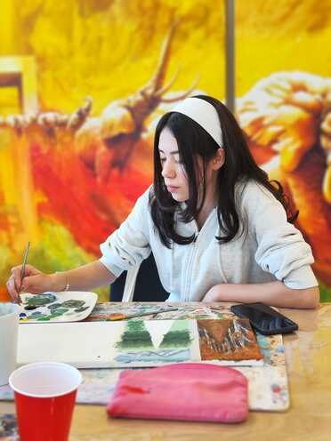 Una adolescente pintando frente a un mural del taller