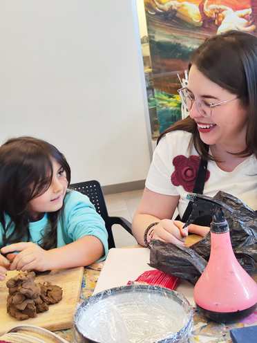 Una maestra acompañando a una niña que trabaja con barro