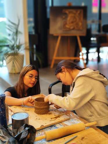 Dos alumnas levantando una pieza de barro