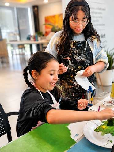 Una alumna pintando de verde mientras una maestra la acompaña