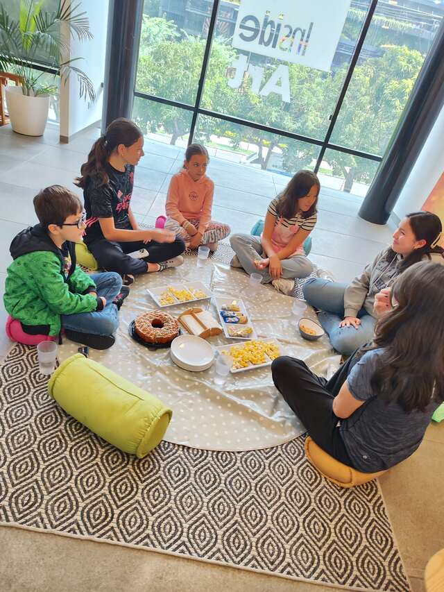Niños sentados en círculo sobre una manta compartiendo la refacción